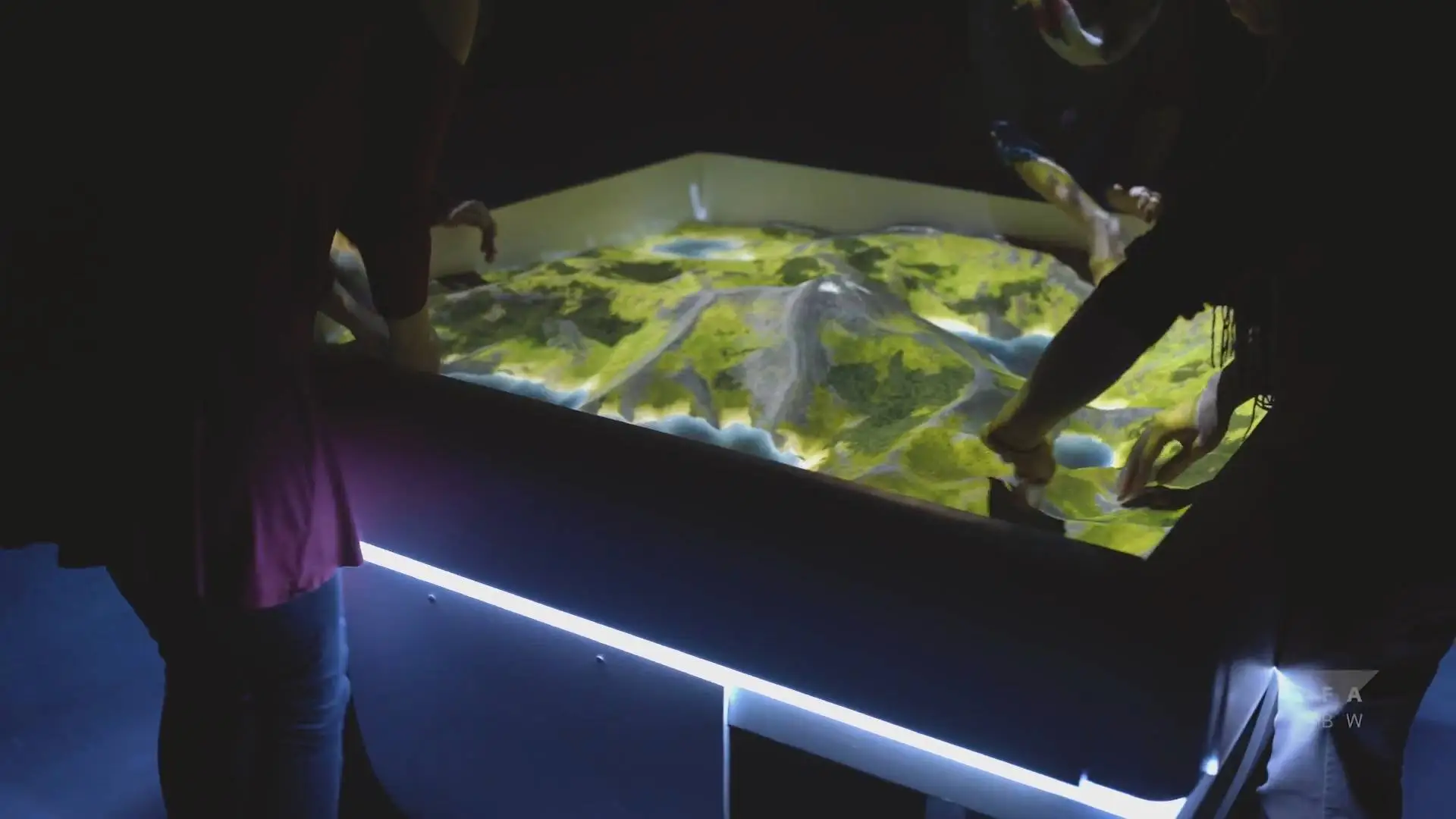 Players shaping the sand while nature is projected onto its surface
